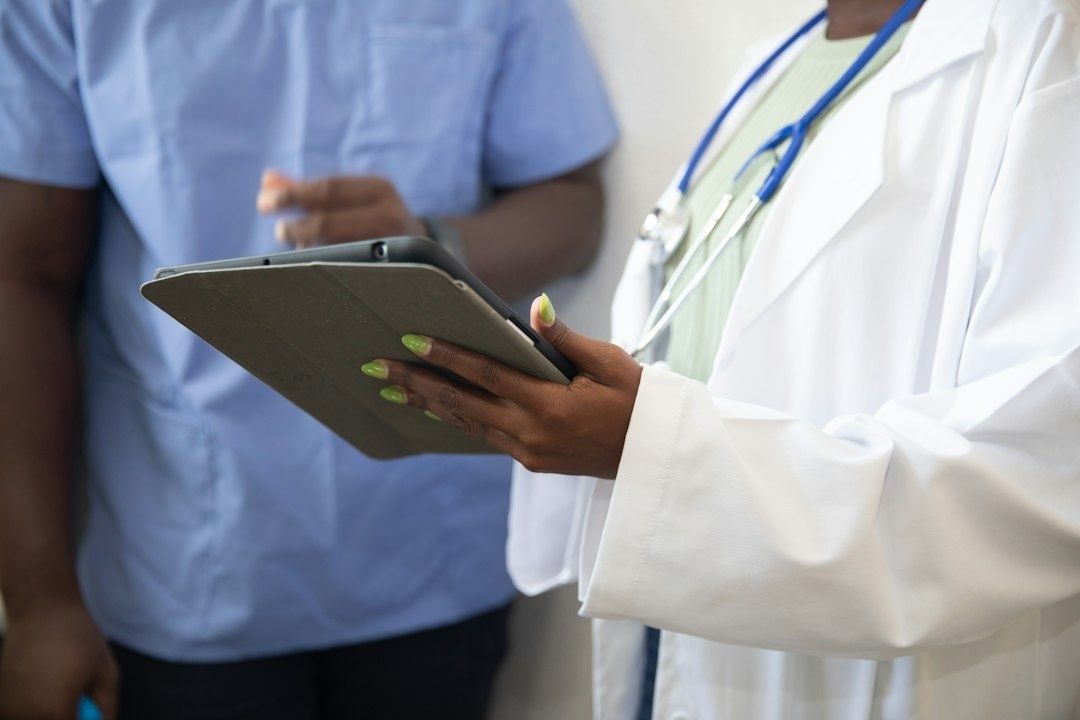 Ärztin mit Stethoskop prüft ein Tablet neben medizinischem Personal